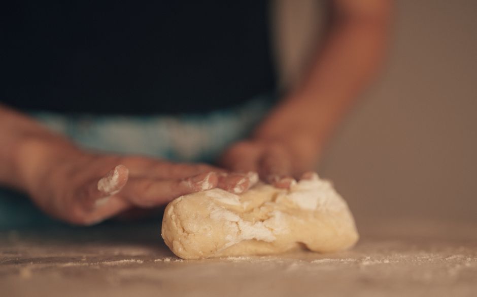 Hands kneading dough on a floured surface in a kitchen setting, focused on baking preparation.