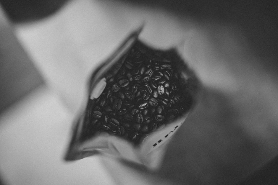 Black and white image capturing coffee beans in a bag from above, providing a moody artistic look.